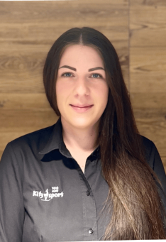 Porträt einer jungen Frau mit einem Kinder-Sportshirt vor einem Holzpaneel-Hintergrund.