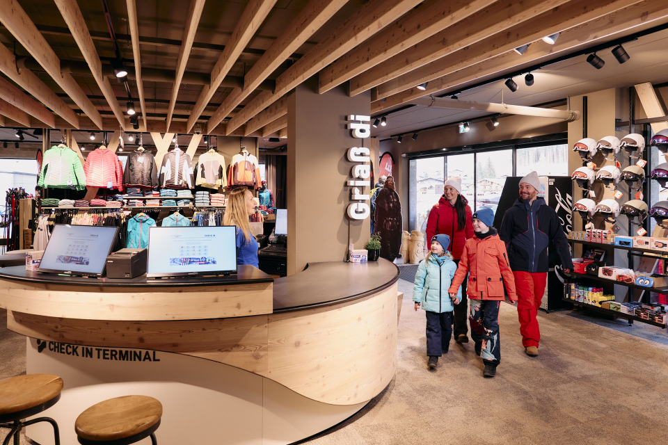 Ski shop interior with a family approaching the checkout counter for winter sports equipment.