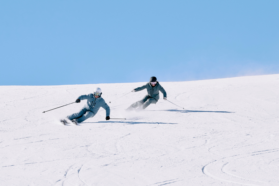 Zwei Skifahrer fahren an einem sonnigen Tag in einem Skigebiet Ski bergab.