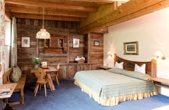 Rustikales Alpenhotelzimmer mit Holzwänden, freiliegenden Balken und gemütlichem Bett.