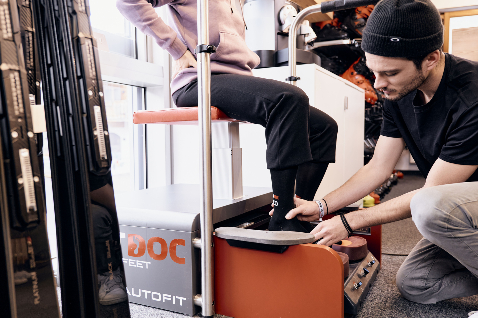 Ein Skiverkäufer passt einem Kunden Skischuhe mit Hilfe einer Bootfitting-Maschine an.