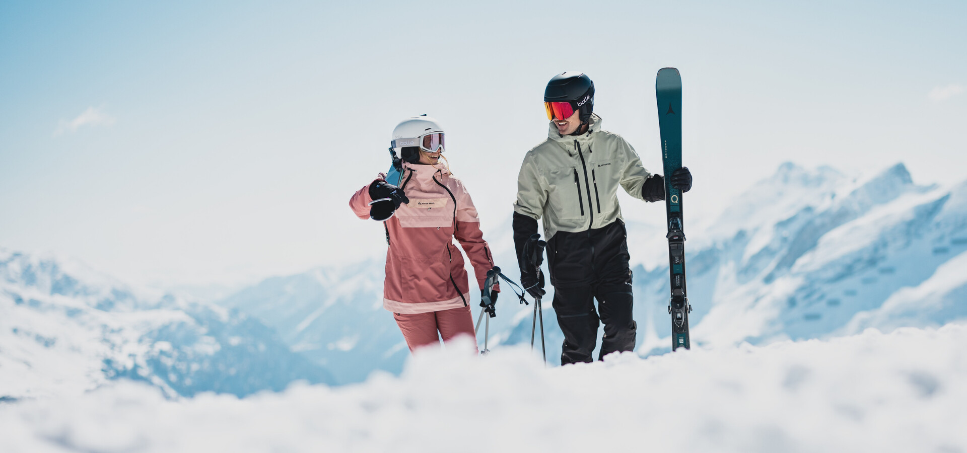 Ein Paar in Skiausrüstung, durchquert tiefen Schnee auf einem sonnigen Alpenberg.