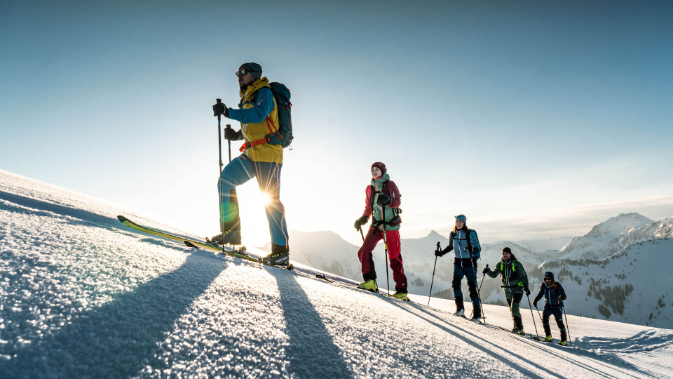 Gruppe von Tourenskifahrern steigt an einem sonnigen Tag einen verschneiten Berghang hinauf.