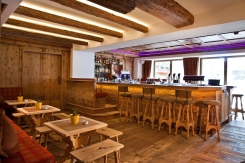 Innenraum einer Skihütten-Bar mit Holzbalken, Hockern, Tischen und Bergblick.