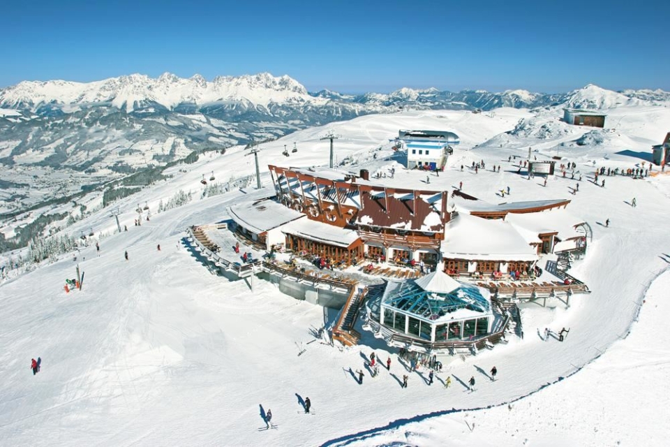 Luftaufnahme eines Skiresorts mit schneebedeckten Gebäuden, Skiliften und einer fernen Bergkette. Wintersportdestination.