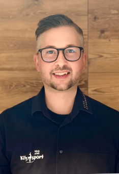 Porträt eines lächelnden Mannes mit Brille, der ein Kitz Sport Poloshirt trägt.