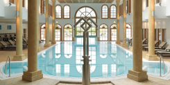 Hallenbad mit Säulen, Bogenfenstern und Liegestühlen in einem luxuriösen Spa-Resort.