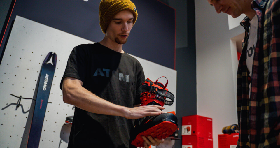 Mann hält Skischuh in einem Geschäft mit Atomic-Skiern. Kauf von Skiausrüstung.