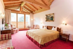 Gemütliches Hotelzimmer mit Kingsize-Bett, Holzdecke, Balkon und einem Gemälde einer Berglandschaft.