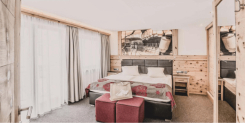 Hotelzimmer-Interieur mit Doppelbett, Holzvertäfelung und Kunstwerken mit Bergmotiven.