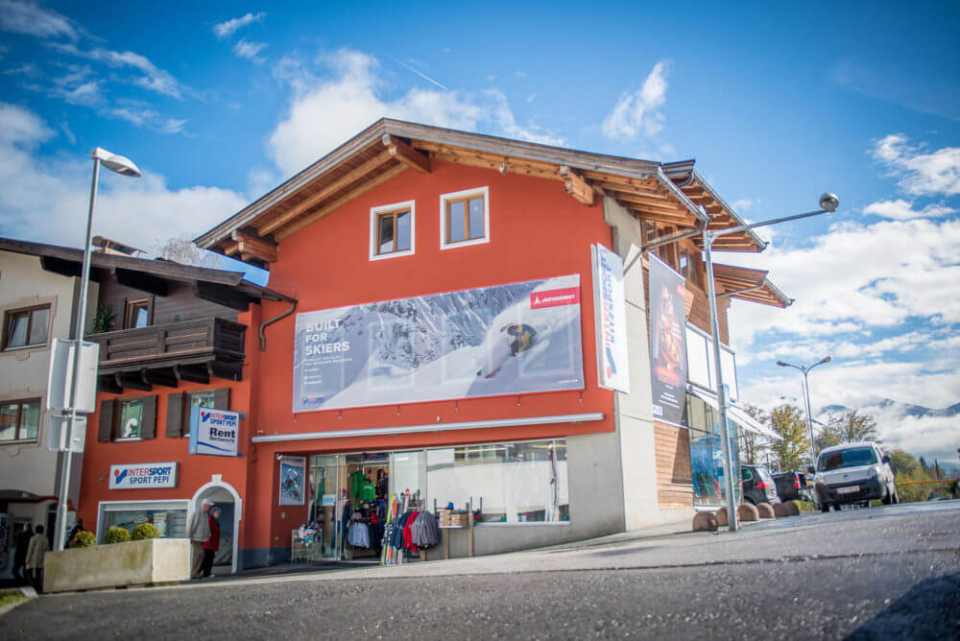 Skigeschäft in den österreichischen Alpen; rotes Gebäude mit Banner für Skiverleih.