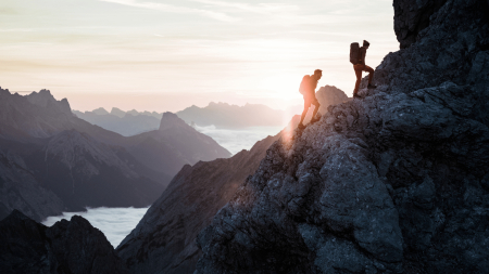 Wanderer besteigen einen felsigen Berggipfel bei Sonnenuntergang; Abenteuerreisen im Gebirge.