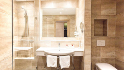 Modernes Badezimmerinterieur mit Marmorfliesen, weißem Waschbecken, Spiegel und Duschkabine.