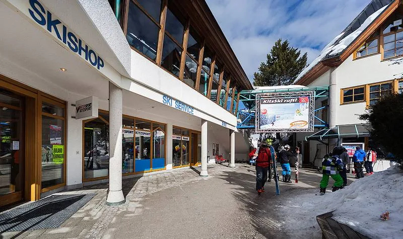 Skigeschäft-Eingang in einem Bergresort mit Skifahrern und Wintersportausrüstung.