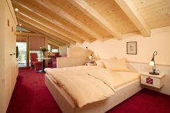 Gemütliches Dachgeschoss-Schlafzimmer-Interieur mit Holzbalkendecke, rotem Teppich und Zugang zum Balkon in einer Hotelsuite.