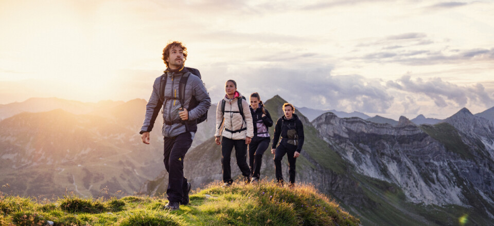 Wanderer besteigen einen felsigen Berggipfel bei Sonnenuntergang; Abenteuerreisen im Gebirge.