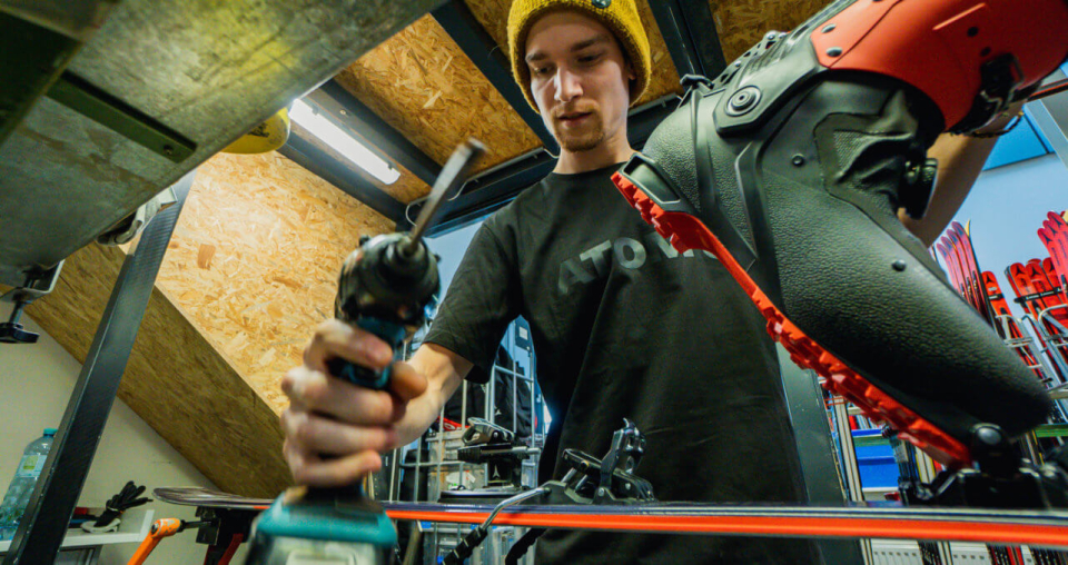 Skitechniker justiert Skibindungen mit einem Akkuschrauber in einer Skiwerkstatt.