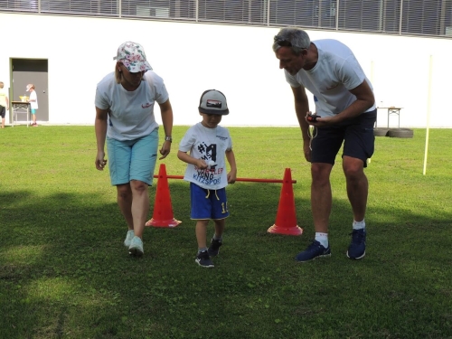 Kind läuft unter Aufsicht eines Erwachsenen einen Hindernisparcours auf einer grünen Wiese. Outdoor-Aktivität für Kinder.