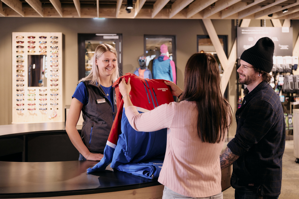 Kunde kauft eine Skijacke in einem Outdoor-Bekleidungsgeschäft mit freundlicher Verkäuferin.