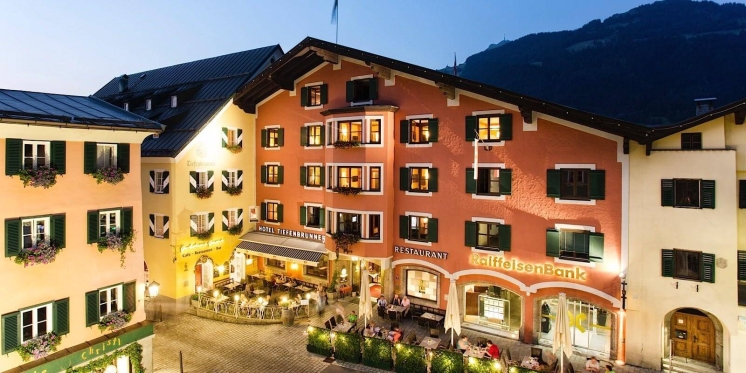 Hotel Zum Hirschen in Österreich, ein traditionelles alpines Gebäude mit Restaurant und Sitzgelegenheiten im Freien in der Abenddämmerung.