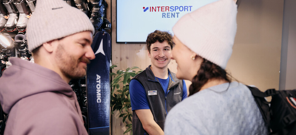 Ein Paar leiht Ski bei Intersport; ein Mitarbeiter des Skiverleihs hilft bei der Skiausleihe.