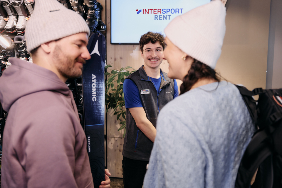Ein Paar leiht Ski bei Intersport; ein Mitarbeiter des Skiverleihs hilft bei der Skiausleihe.